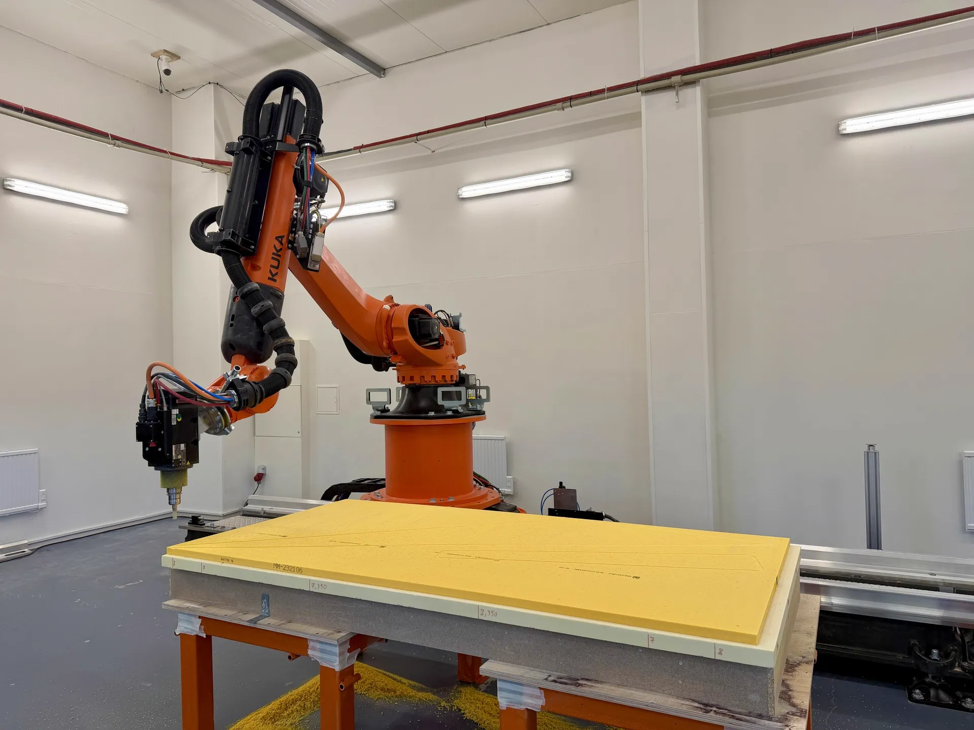 KUKA industrial robot milling a yellow material block on a work table in a manufacturing facility